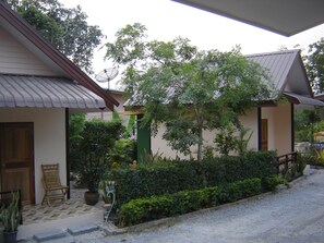 A building with a tiled entrance, a wooden door, and a small porch with a chair and potted plants. - Numhom Resort (Thap Than)