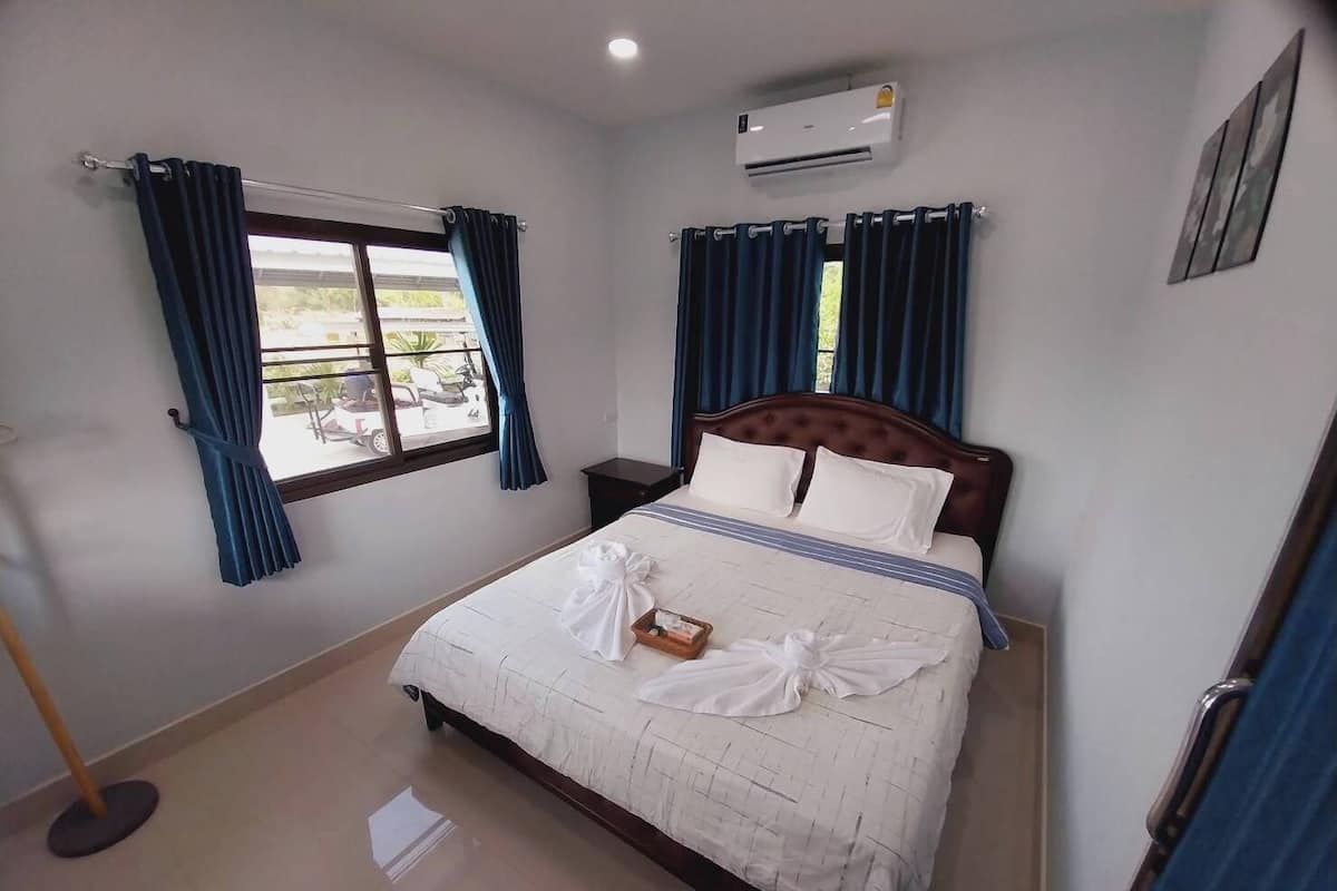 A hotel room with a bed, a window with curtains, an air conditioning unit, and a tiled floor.