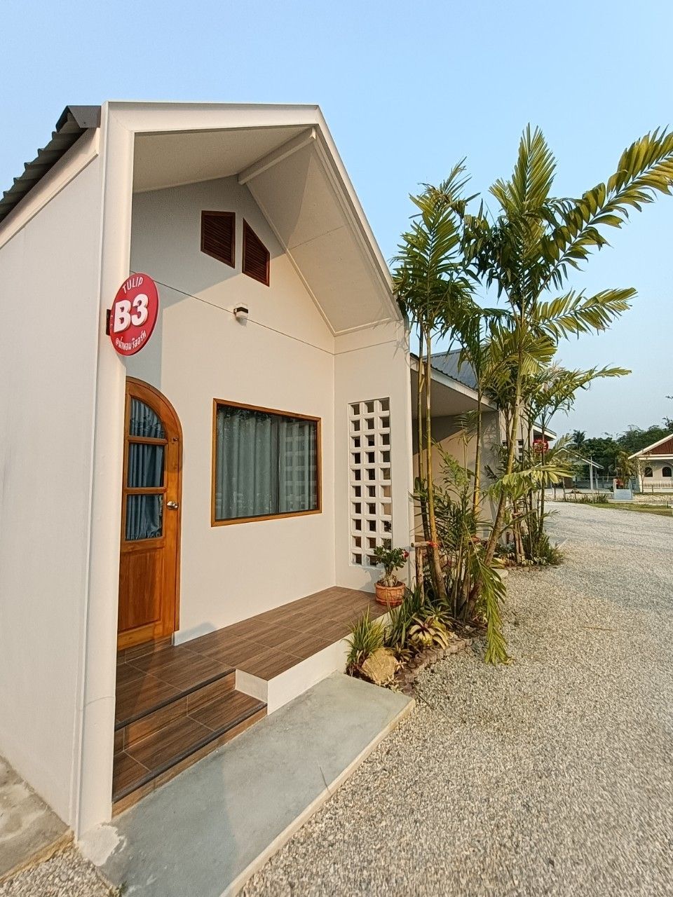 A modern house with a wooden door, a window with curtains, and a small porch area with plants.