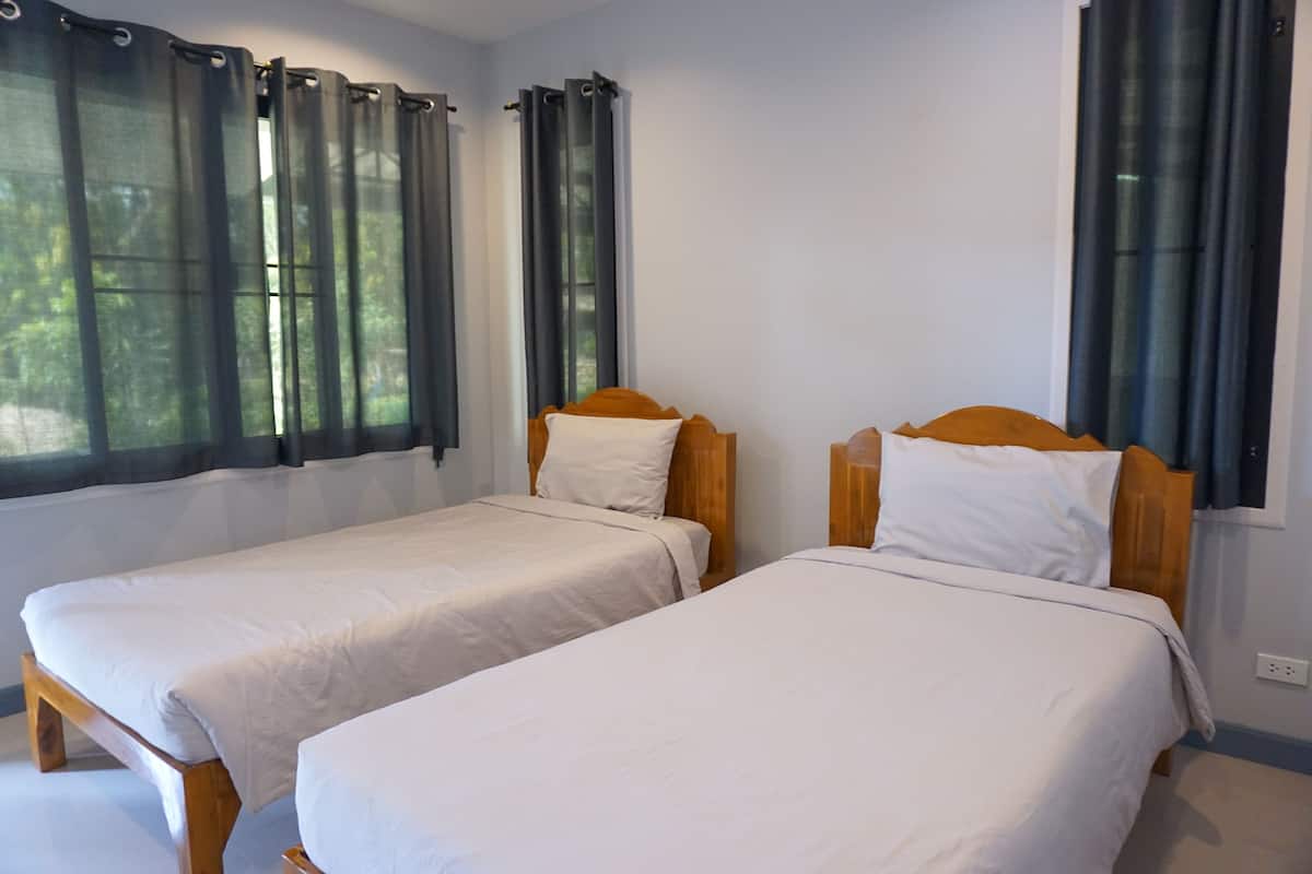 Two single beds with wooden headboards and white bedding in a room with large windows and curtains.