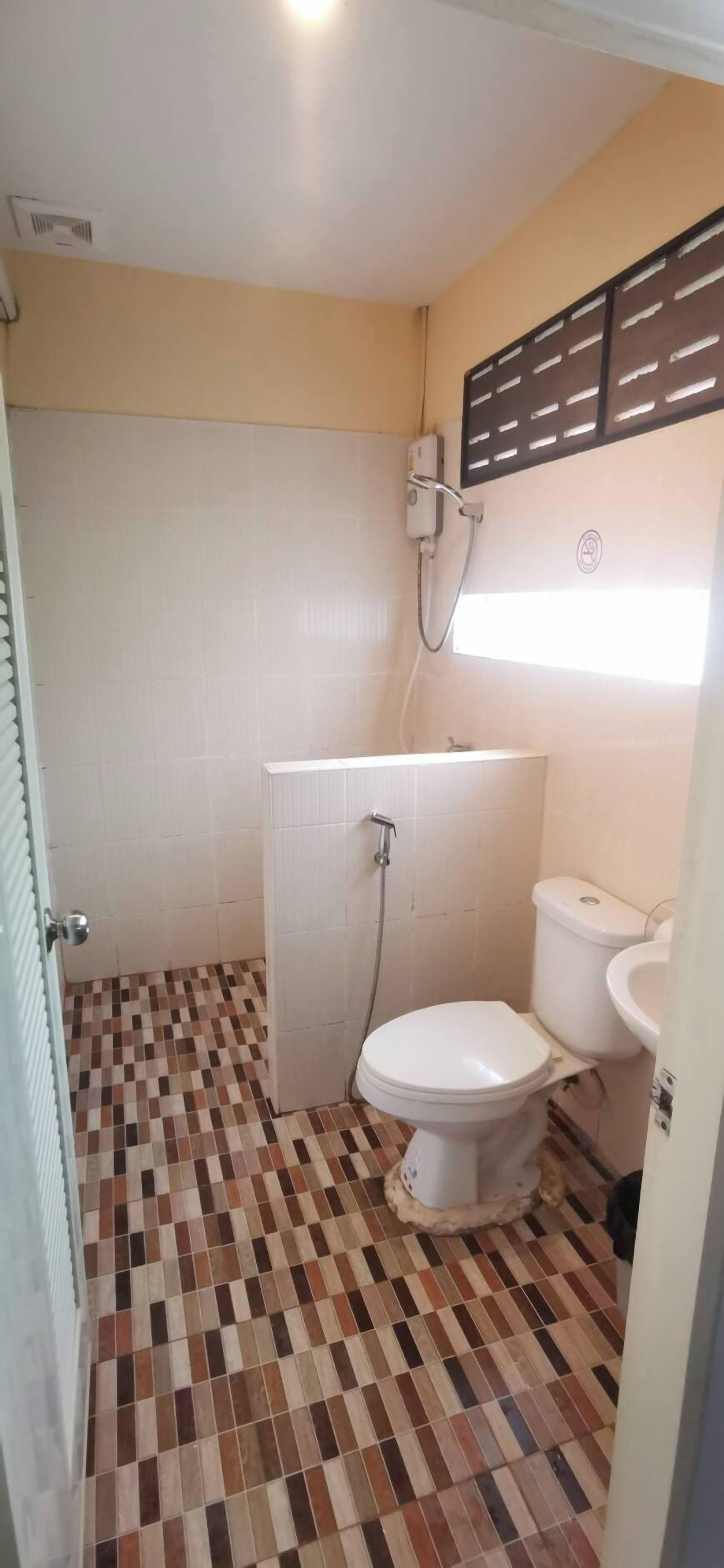 A small bathroom with a toilet, sink, and shower. The floor has a checkered tile pattern.