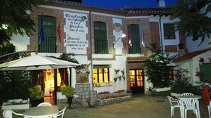 A courtyard with outdoor seating, a building with a sign, and a brick facade. - Gran Posada La Mesnada (Olmedo)