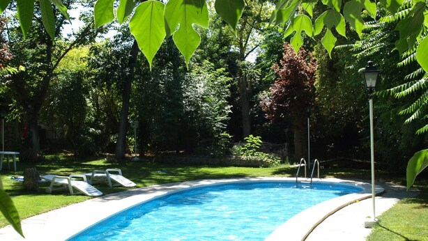 A swimming pool with clear blue water, surrounded by a grassy area and trees. - Gran Posada La Mesnada (Olmedo)