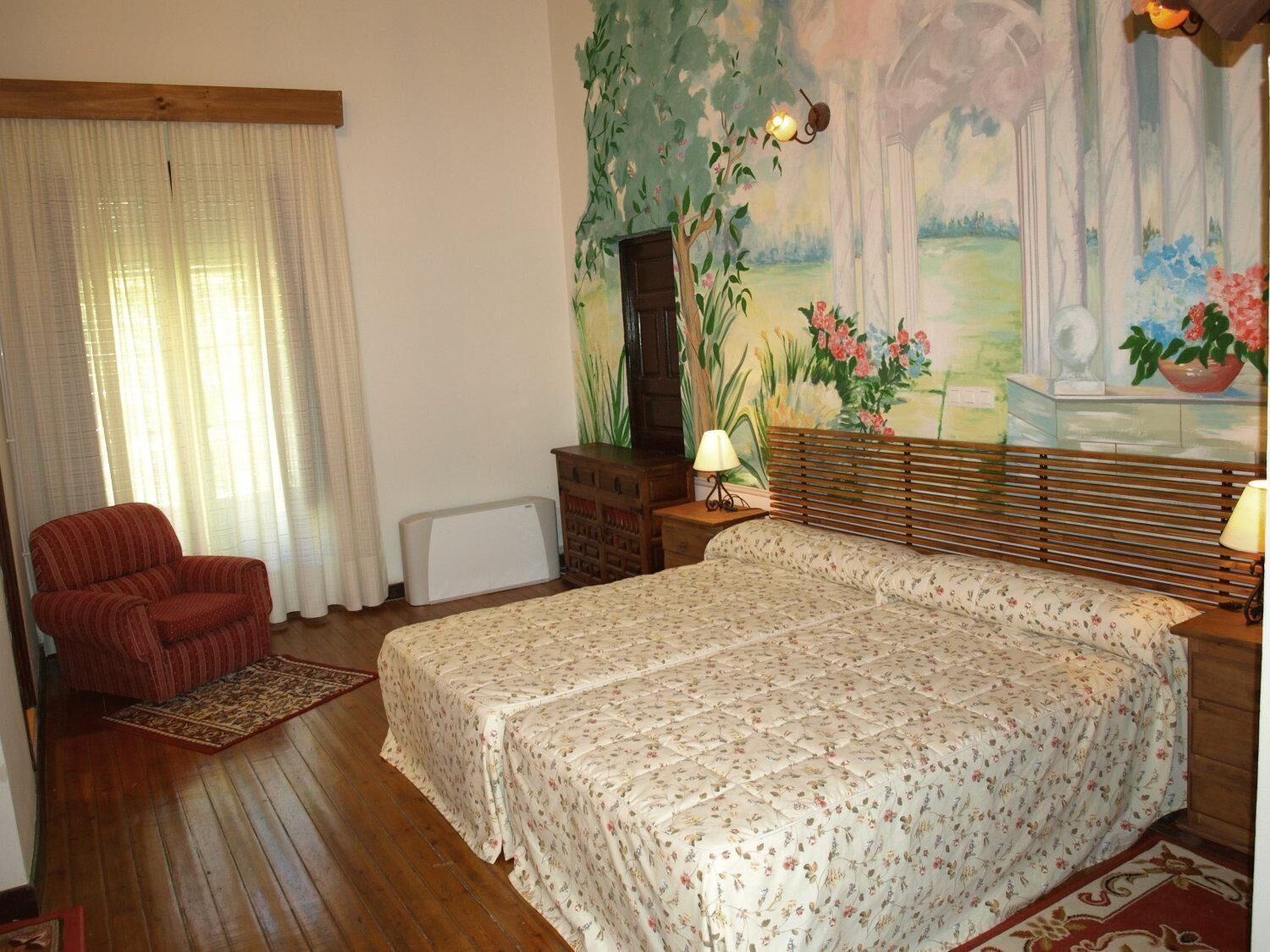Un dormitorio con una cama grande, una silla, un radiador, una lámpara y una pared decorada con un mural floral.