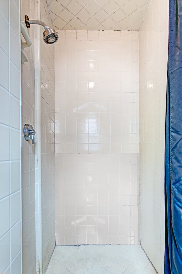 A small, tiled shower with a handheld showerhead and a wall-mounted faucet.