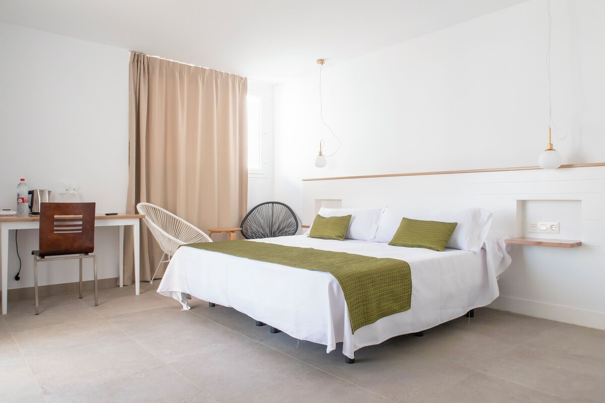 A modern hotel room with a bed, a desk, a chair, and a small shelf.