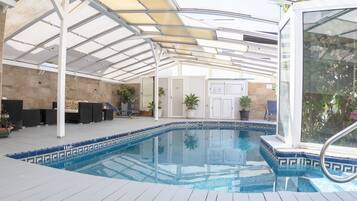 Una piscina interior con techo de cristal, suelo de baldosas y plantas en macetas.
