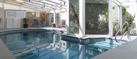 Un área de piscina con agua azul cristalina, un jacuzzi con paredes de vidrio y plantas en macetas.