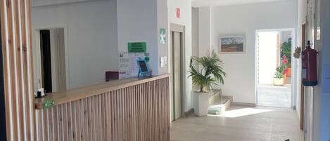 Un área de recepción con un mostrador de madera, un letrero para recepción y conserjería, una planta y un extintor.
