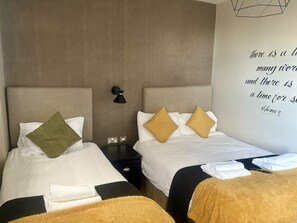 A hotel room with two beds, each with white linens and decorative pillows. There is a wall-mounted lamp between the beds, and a quote on the wall. - The White Swan (Leeds)