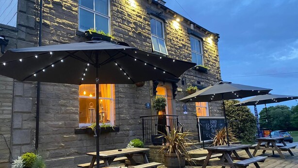 A stone building with outdoor seating and string lights. - The White Swan (Leeds)