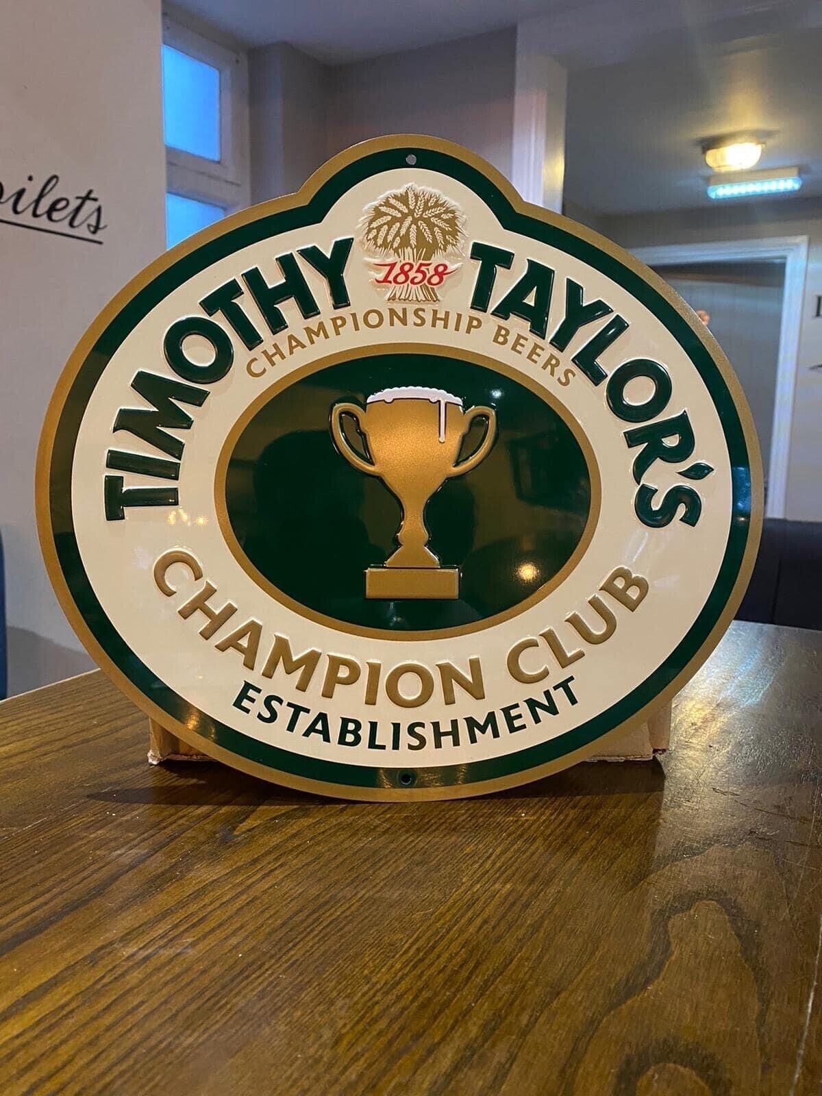 A circular sign with the text "Timothy Taylor's Championship Beers Champion Club Establishment" and a trophy icon.