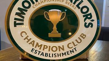A circular sign with the text "Timothy Taylor's Championship Beers Champion Club Establishment" and a trophy icon.