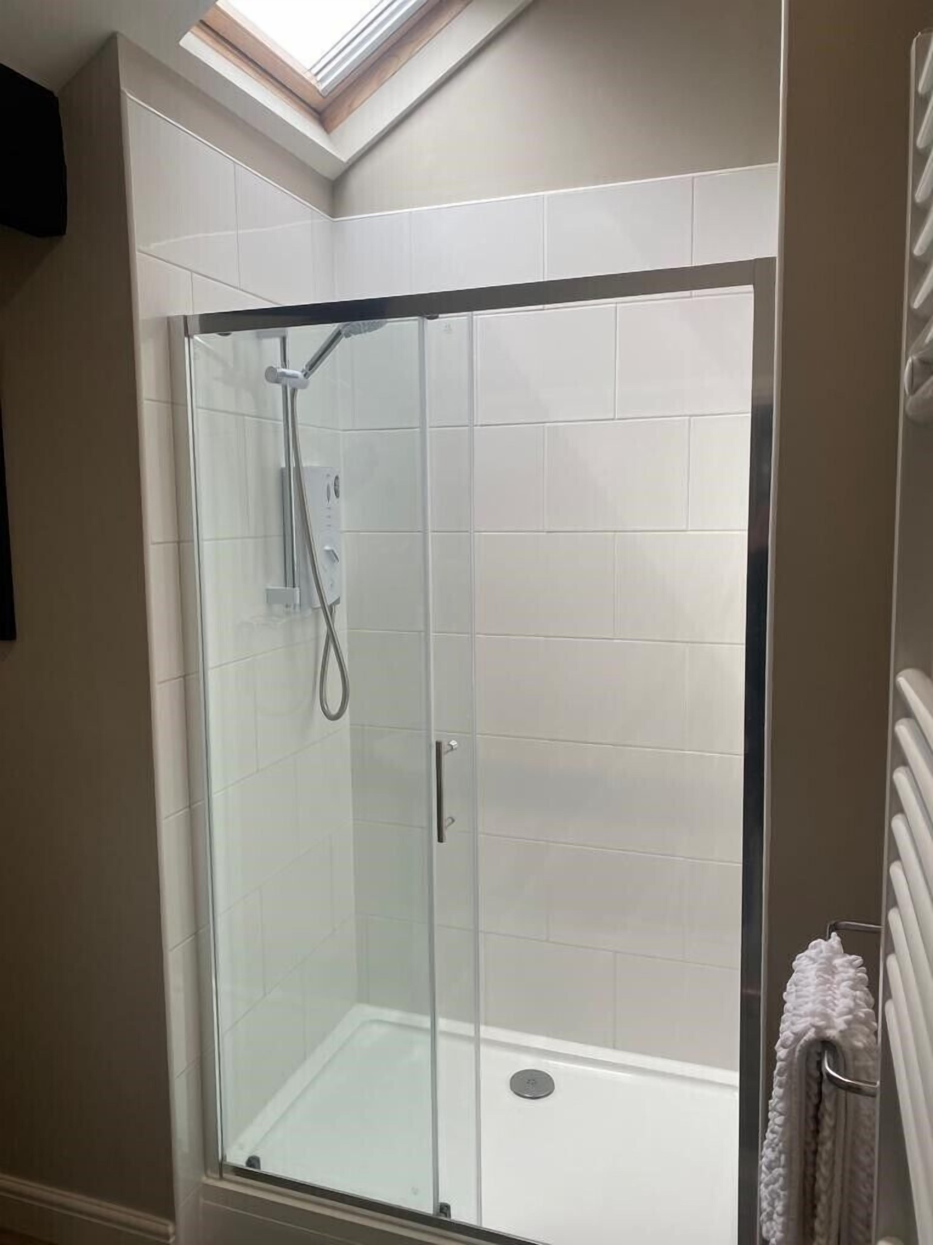 A glass-enclosed shower with a skylight, white tiled walls, and a towel rack.
