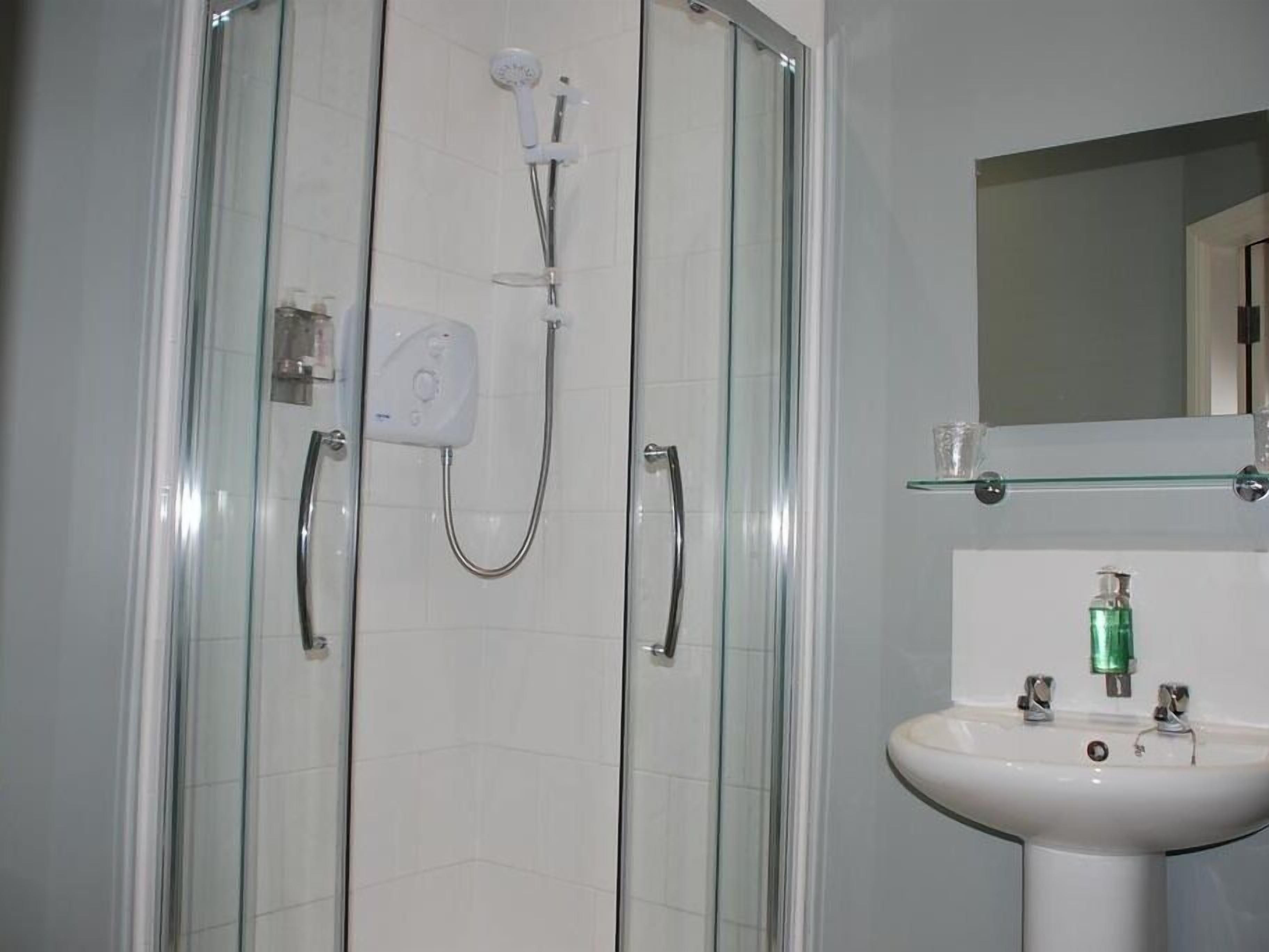Un baño moderno con ducha vidriada, lavamanos blanco y espejo encima.