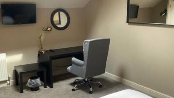 A bedroom with a bed, a desk, a chair, a TV, and a mirror.