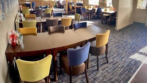 A hotel dining area with multiple tables and chairs, a patterned wall, and large windows. - The White Swan (Leeds)