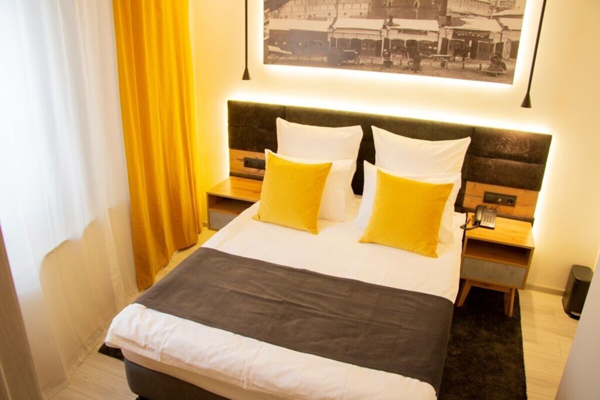 A neatly made bed with white and yellow pillows, a dark headboard, and a bedside table with a lamp.