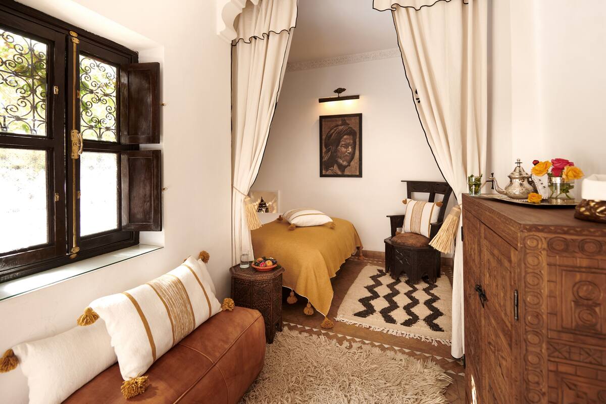 Un dormitorio con cama, un armario de madera, una ventana con cortinas, una alfombra y un cuadro colgado en la pared.