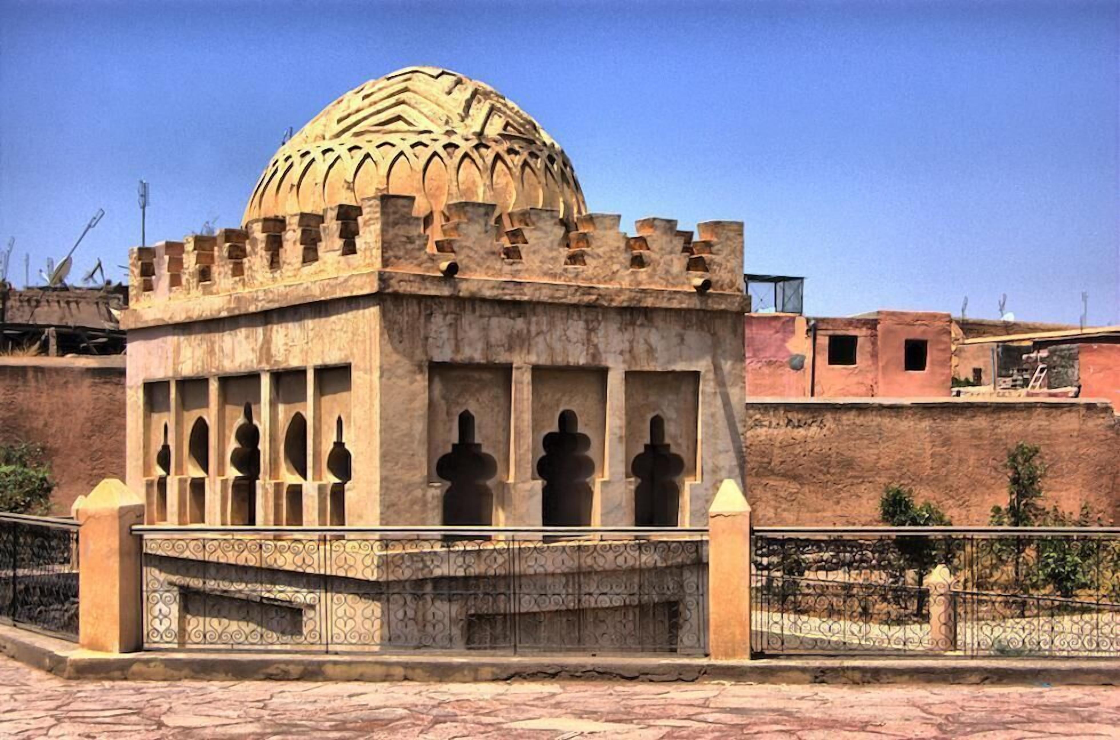 A historical building with a dome and arched windows, surrounded by a fence and a paved area.