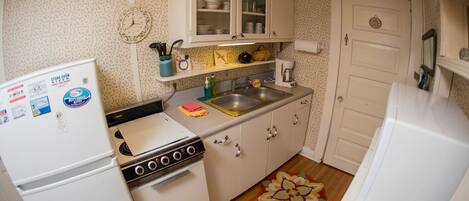 A compact kitchen with a refrigerator, stove, and sink. There are cabinets above the sink and a clock on the wall.