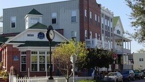 A multi-story building with a clock on the corner, a white picket fence, and parked cars along the street.
