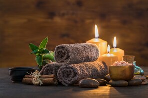 Un espace de bien-être avec des serviettes roulées, des bougies et un bol de sels de bain roses.