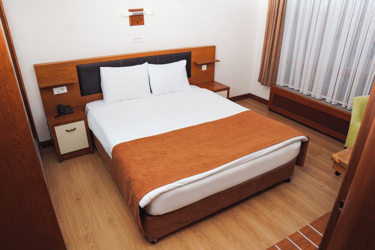Een hotelkamer met een groot bed, een houten hoofdbord, nachtkastjes, een telefoon en een raam met gordijnen.