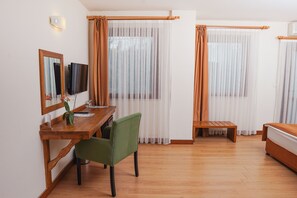 Une pièce avec un bureau en bois, une chaise verte, un lit et deux fenêtres avec des rideaux.