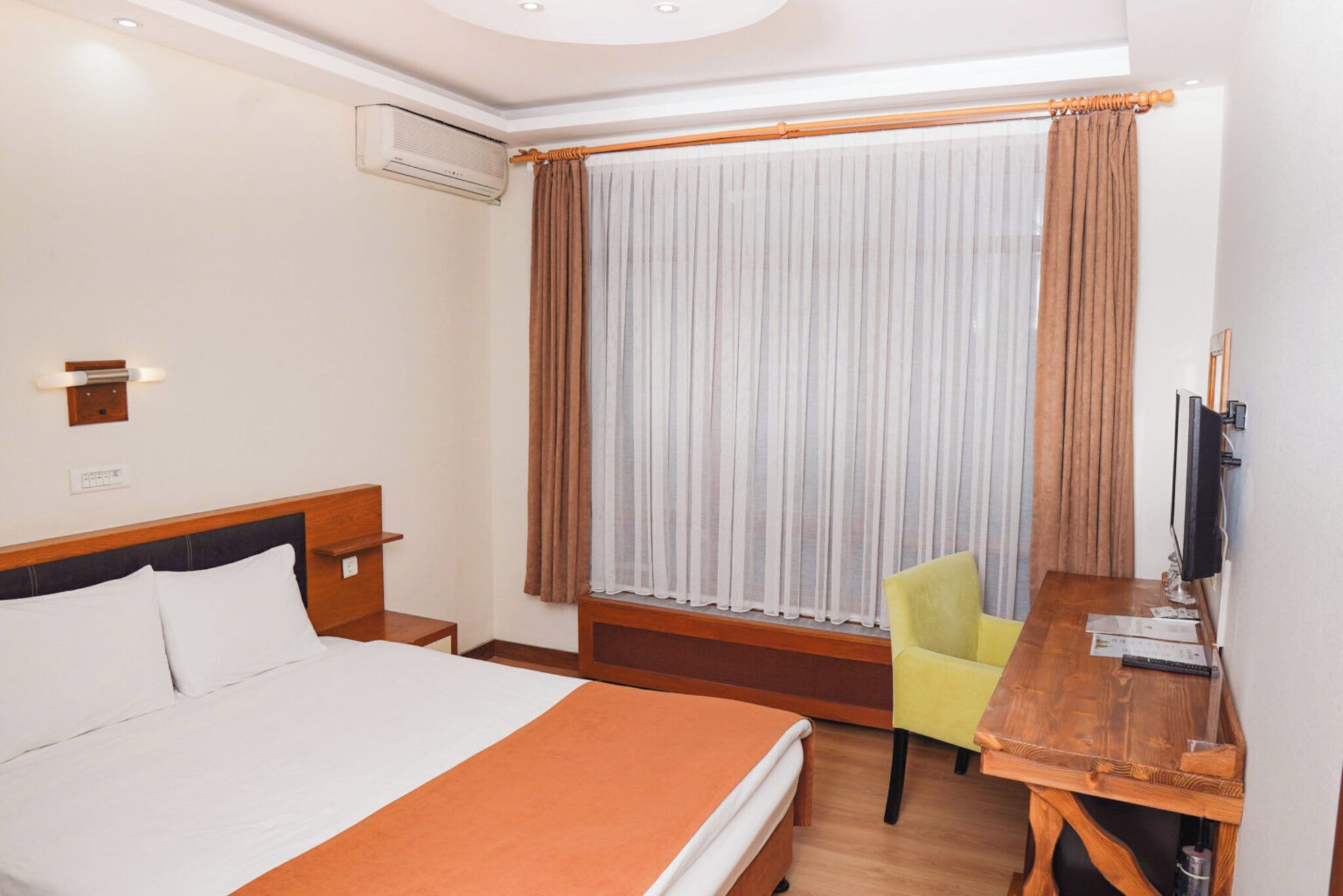 Ein Hotelzimmer mit Bett, Schreibtisch, Stuhl, Fernseher und einem fensterbepflanzten Fenster.