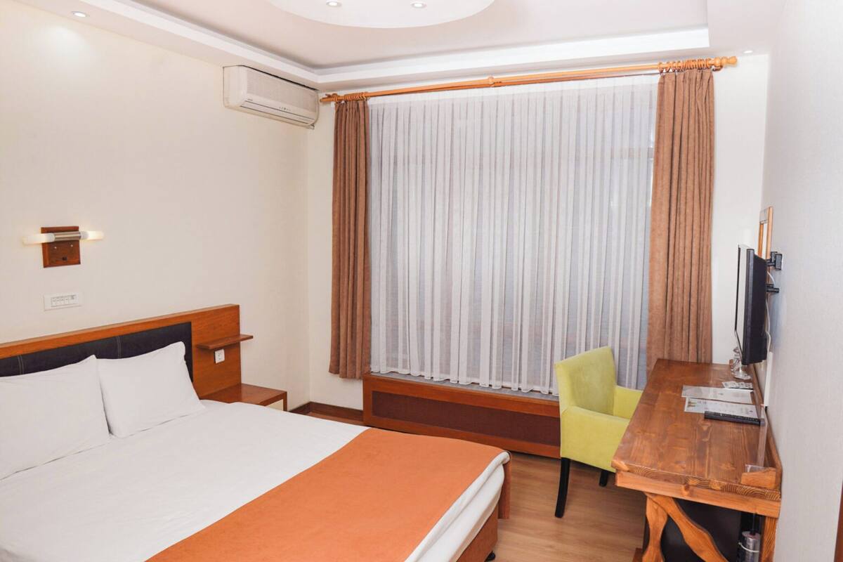 A hotel room with a bed, a desk, a chair, a television, and a window with curtains.