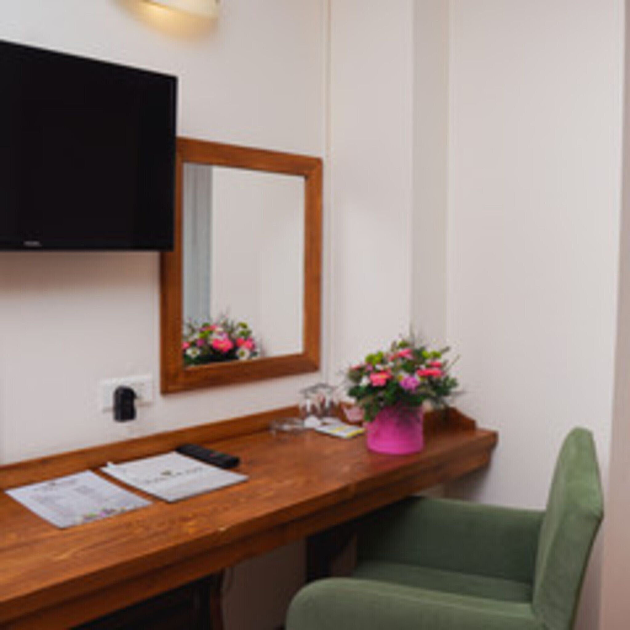 Ein Zimmer mit einem Holztisch, einem Spiegel, einer rosa Blumenvase und einem grünen Stuhl.