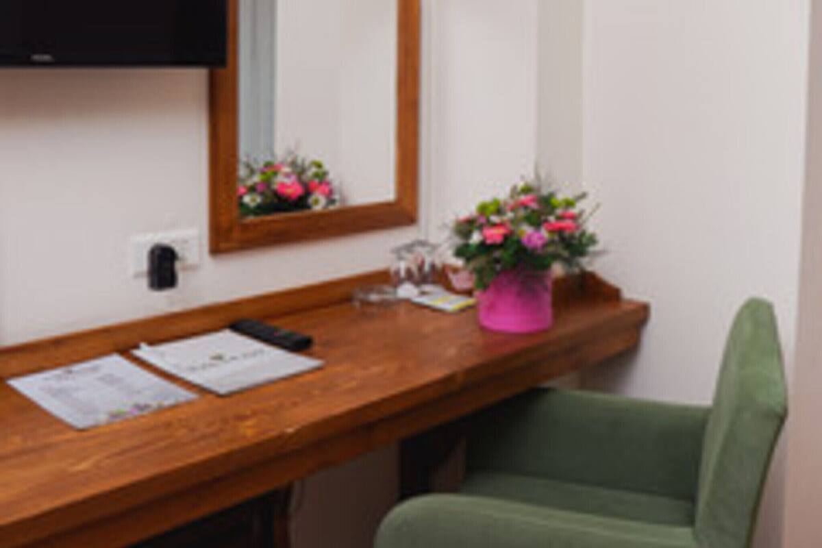 A room with a wooden desk, a mirror, a pink flower vase, and a green chair.