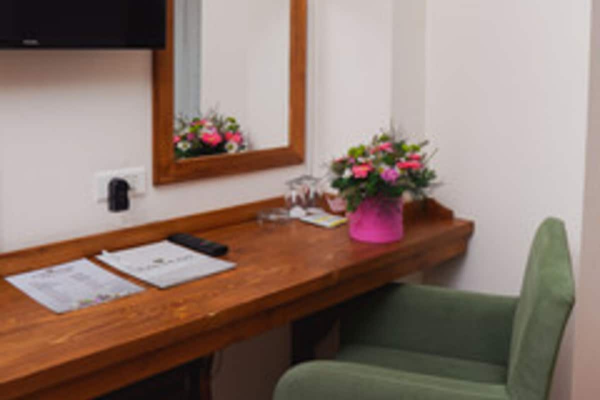 Ein Zimmer mit einem Holztisch, einem Spiegel, einer rosa Blumenvase und einem grünen Stuhl.