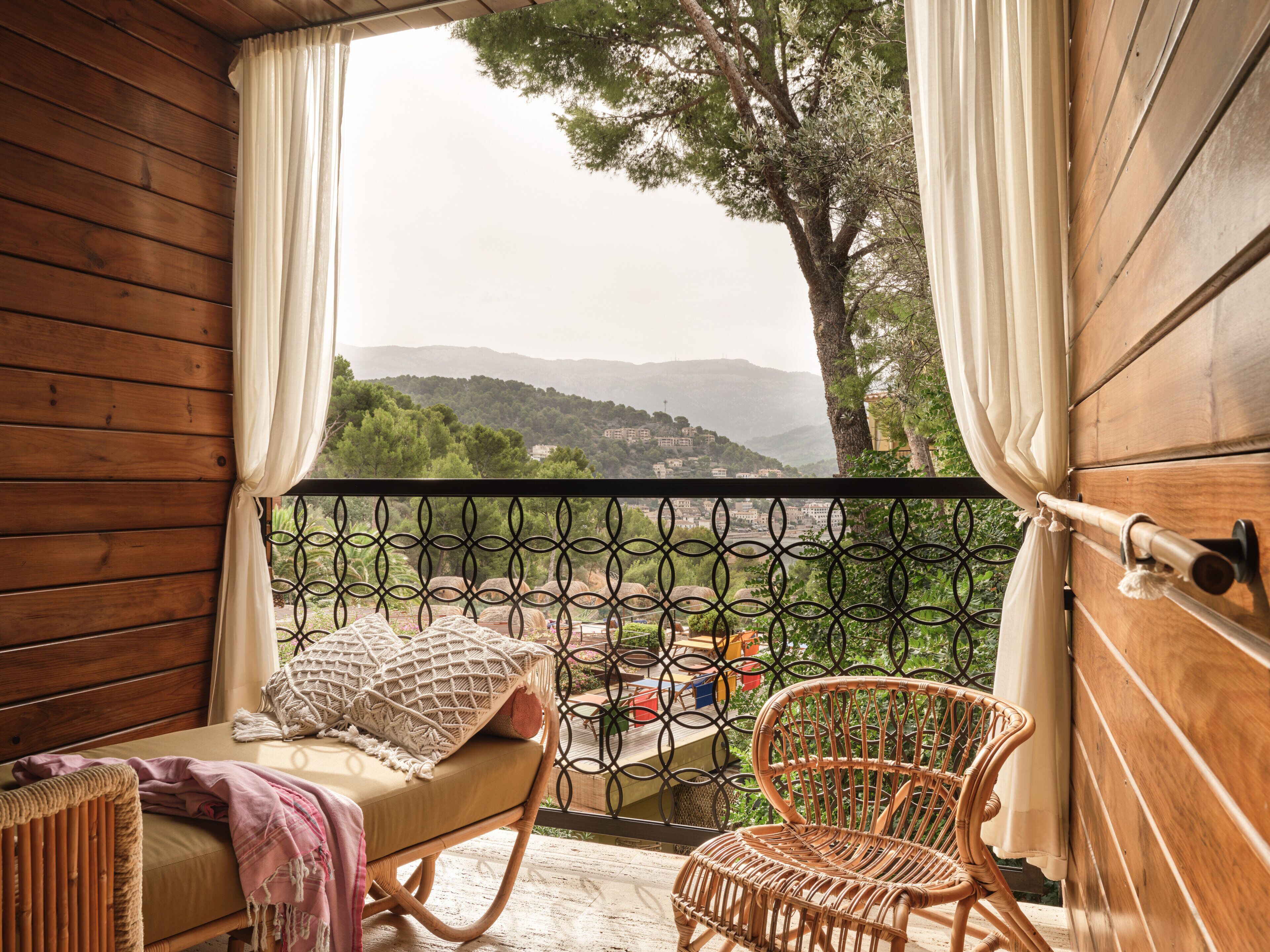 Un balcon en bois agrémenté de meubles en osier, avec vue sur des collines et une balustrade.
