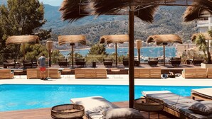 A poolside area with lounge chairs and umbrellas, overlooking a body of water and a mountainous landscape.
