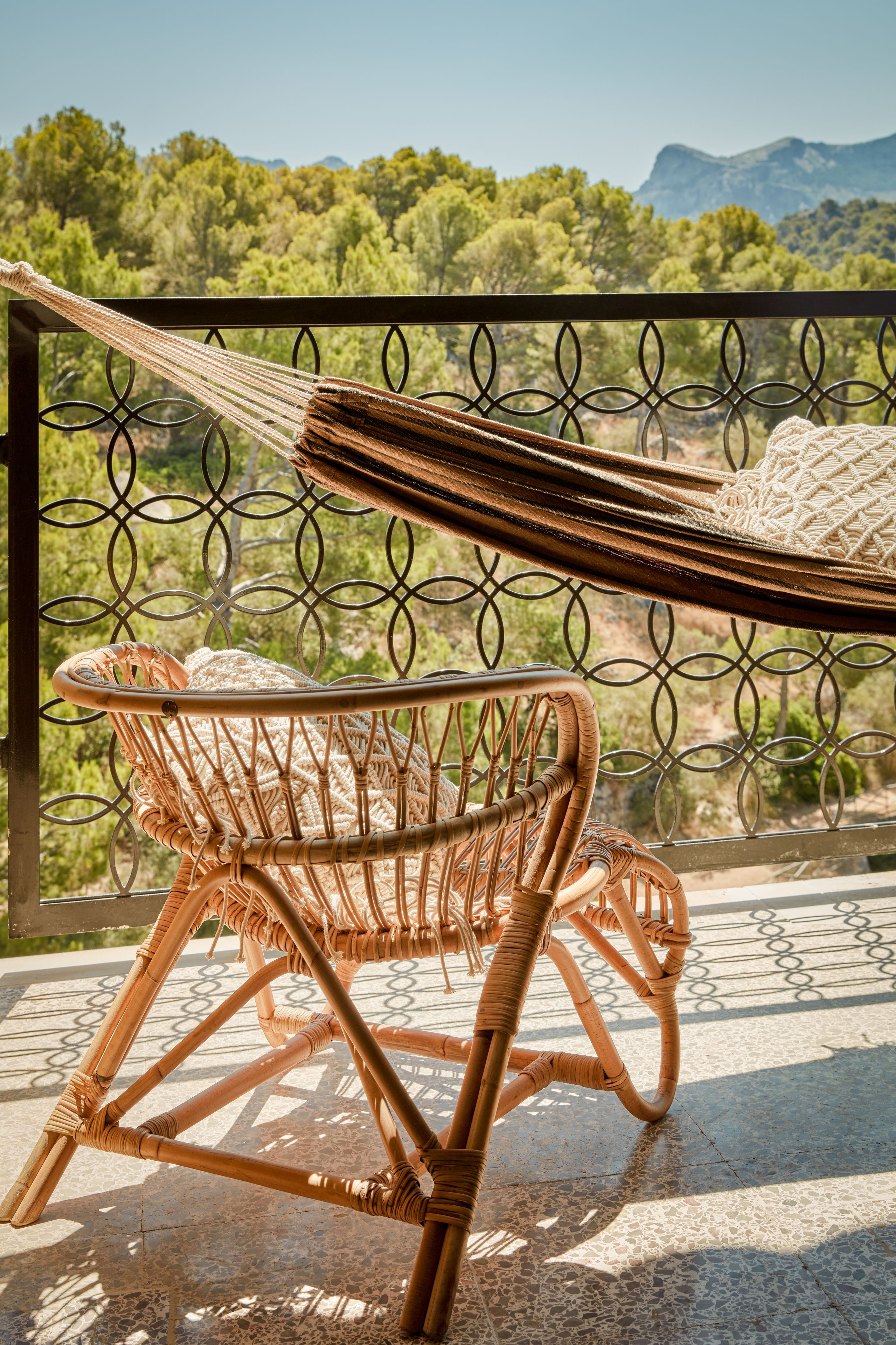 A wicker chair with a hammock on a balcony with a metal railing, overlooking a forested landscape.