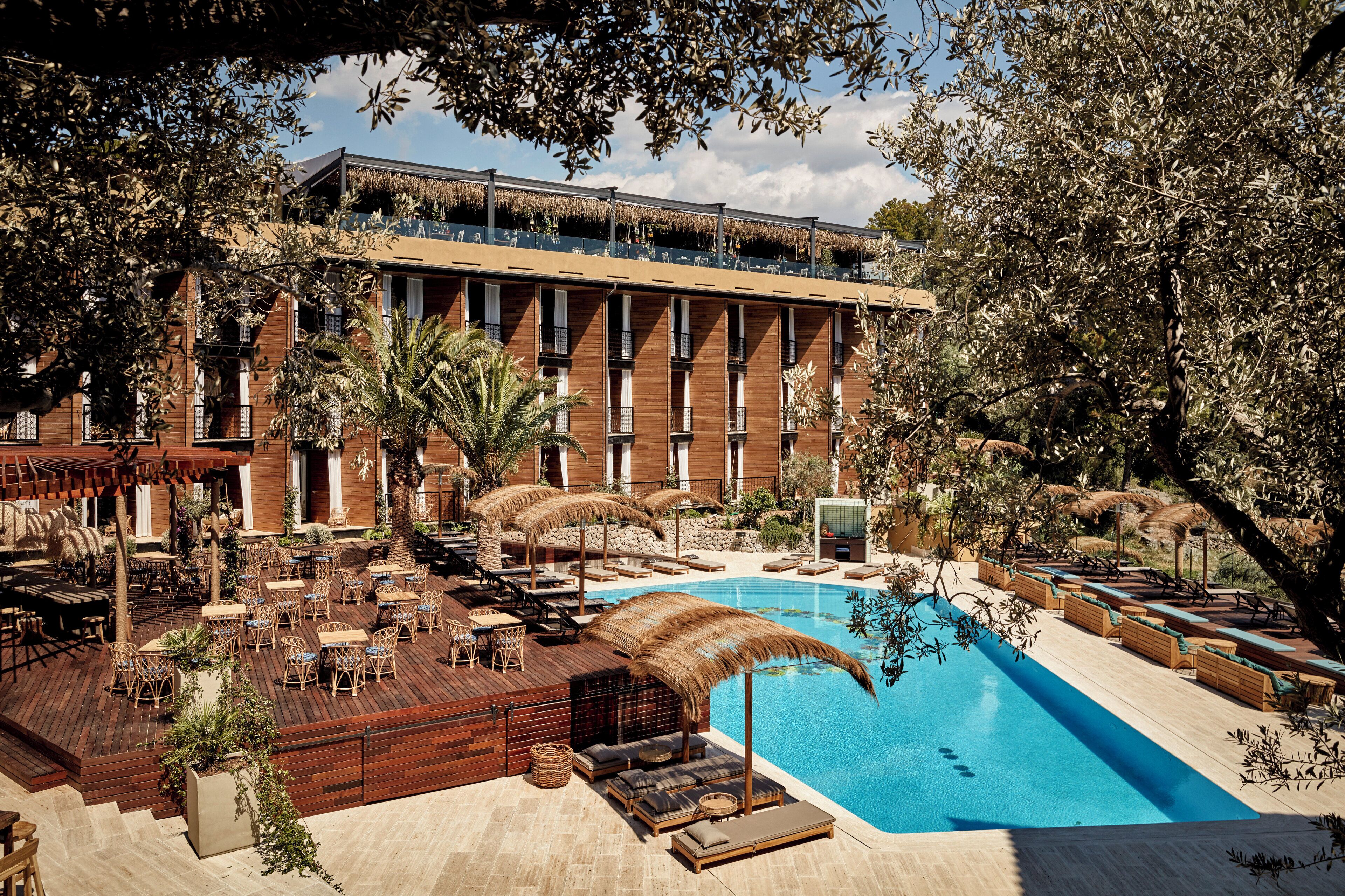 A resort with a swimming pool, outdoor seating, and a building with multiple windows.