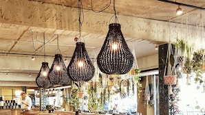 A spacious restaurant with a long wooden table, multiple hanging pendant lights, and a rustic ceiling.