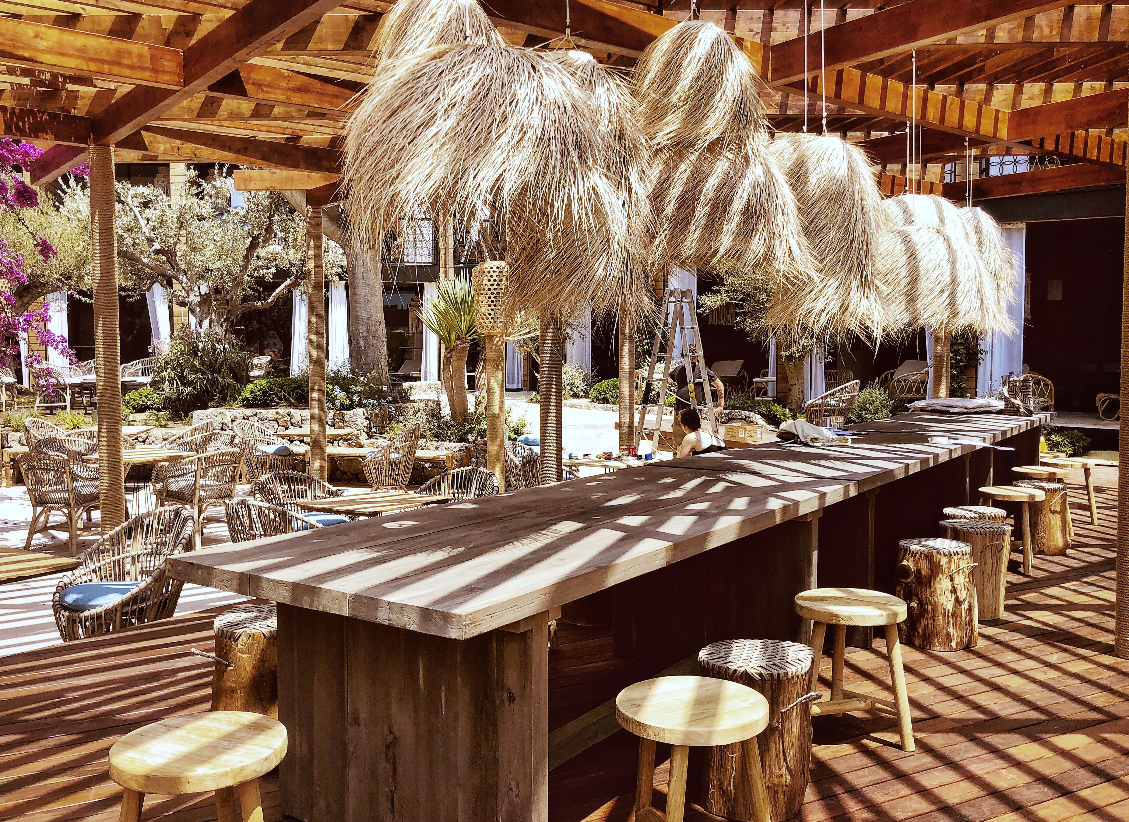 An outdoor dining area with a long wooden table, wicker chairs, and thatched umbrellas.