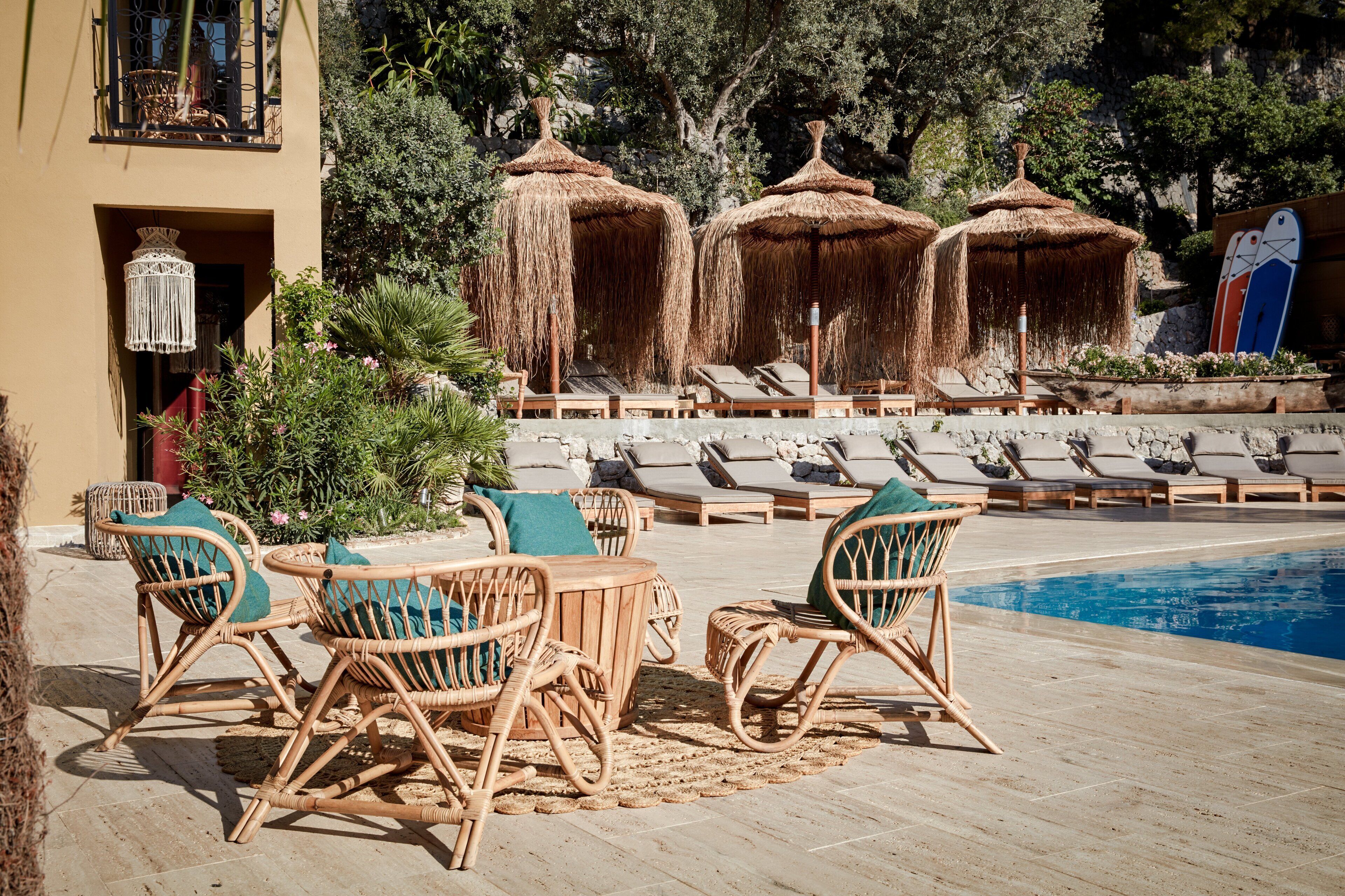 A poolside area with lounge chairs, a table, and thatched umbrellas.