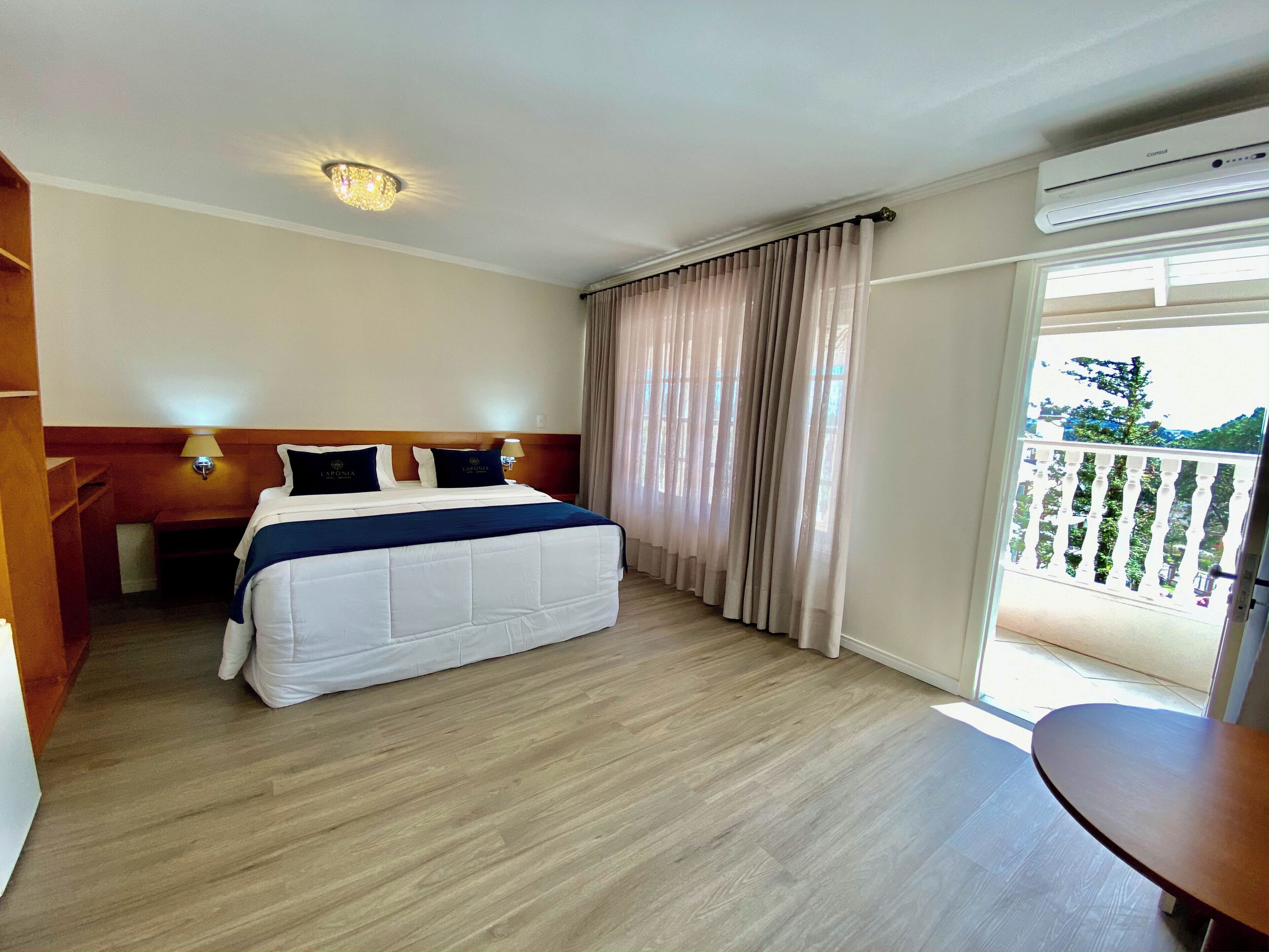 A hotel room with a bed, bedside lamps, a wooden headboard, a balcony with a view, and an air conditioning unit.