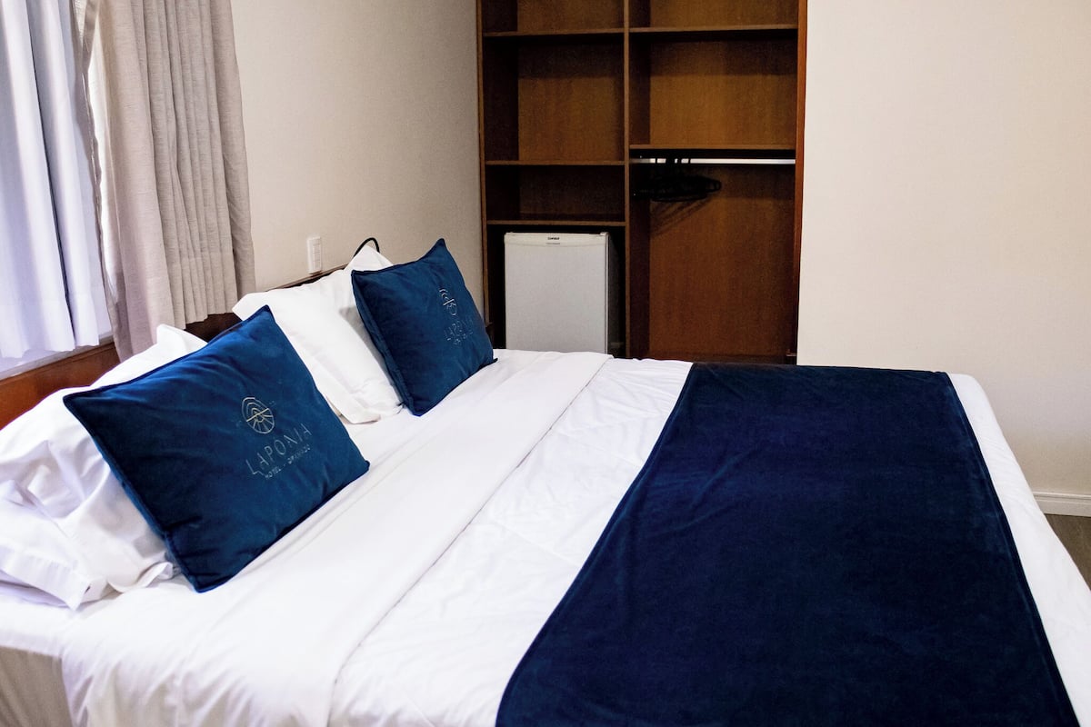 A bed with white and blue bedding, a small white appliance, and a wooden wardrobe.