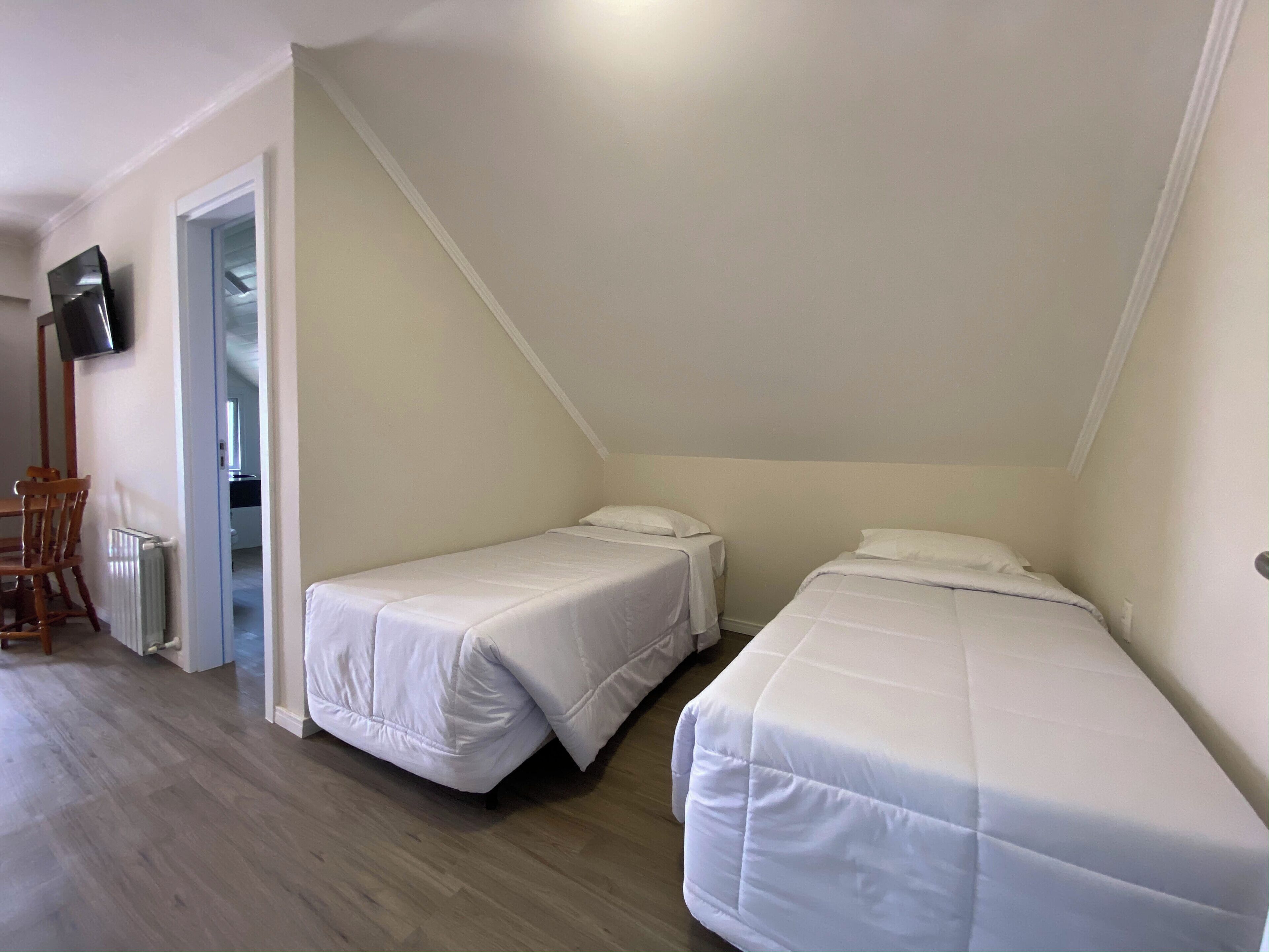 Een kamer met twee eenpersoonsbedden, een houten stoel, een bureau en een aan de muur bevestigde televisie.