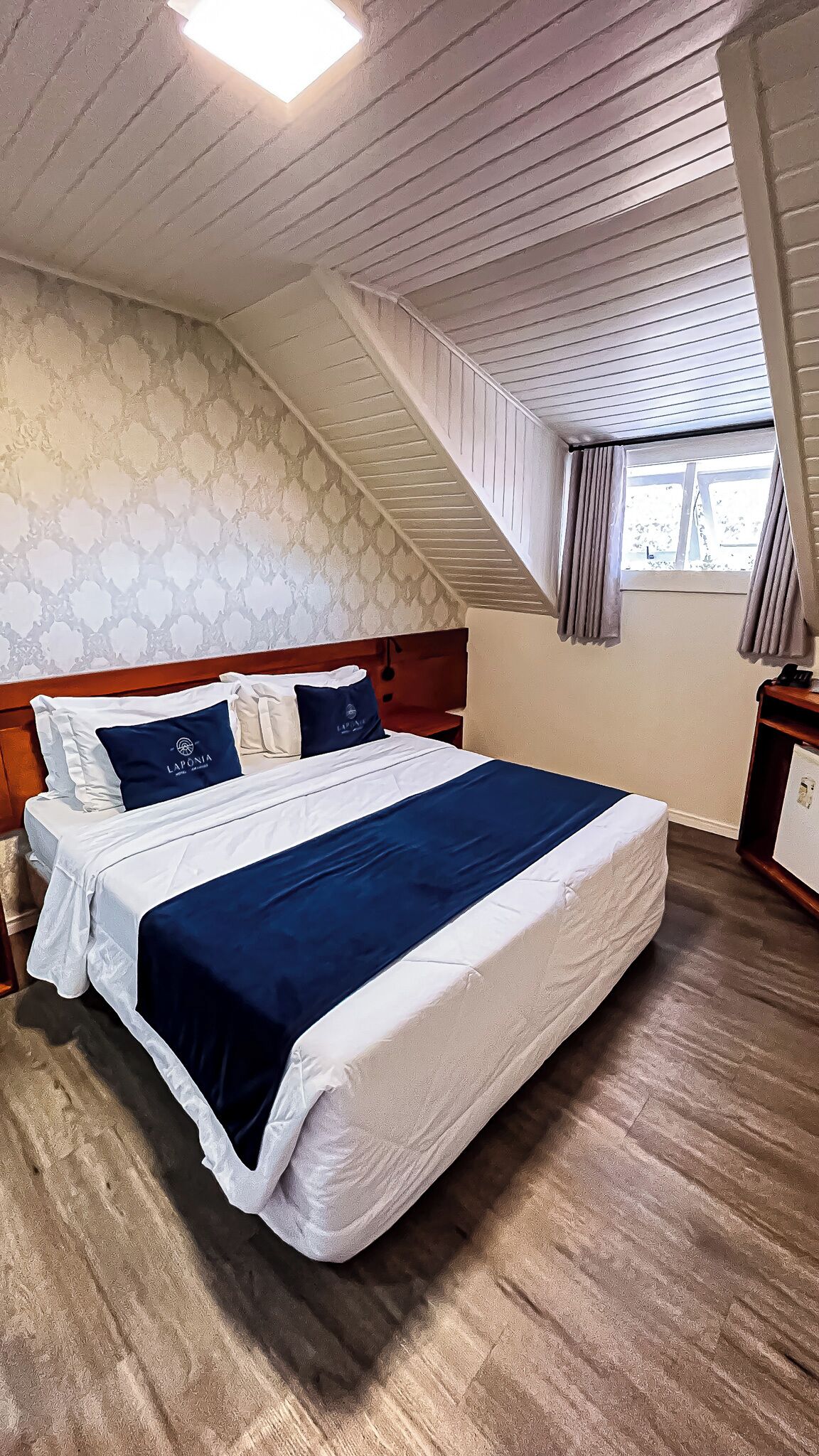 Une chambre à coucher avec un lit, une tête de lit en bois, un mur à motifs et une fenêtre avec des rideaux.