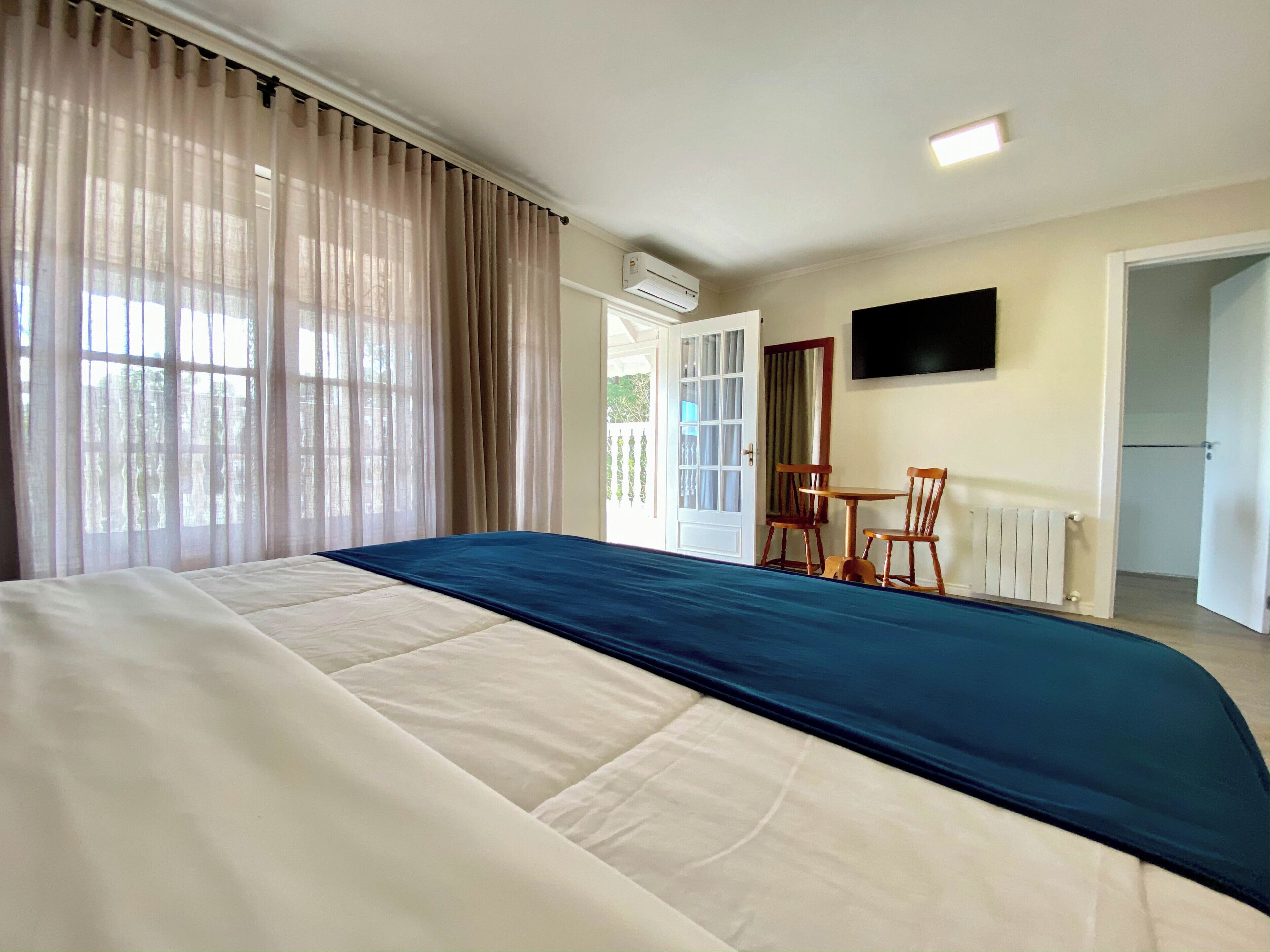 Une chambre d’hôtel dotée d’un grand lit, d’un coin repas avec des chaises, d’un téléviseur fixé au mur et d’un appareil de climatisation.