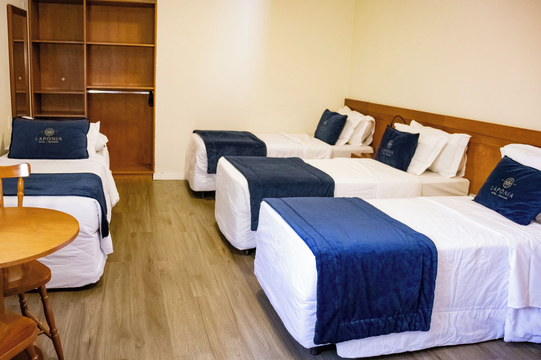 Camera d'albergo con tre letti, un'armadiatura in legno e un tavolino rotondo.