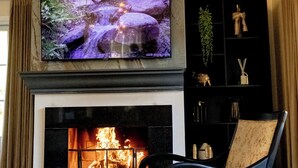 Een woonkamer met een open haard, een televisie erboven en een stoel met een gestreept kussen.