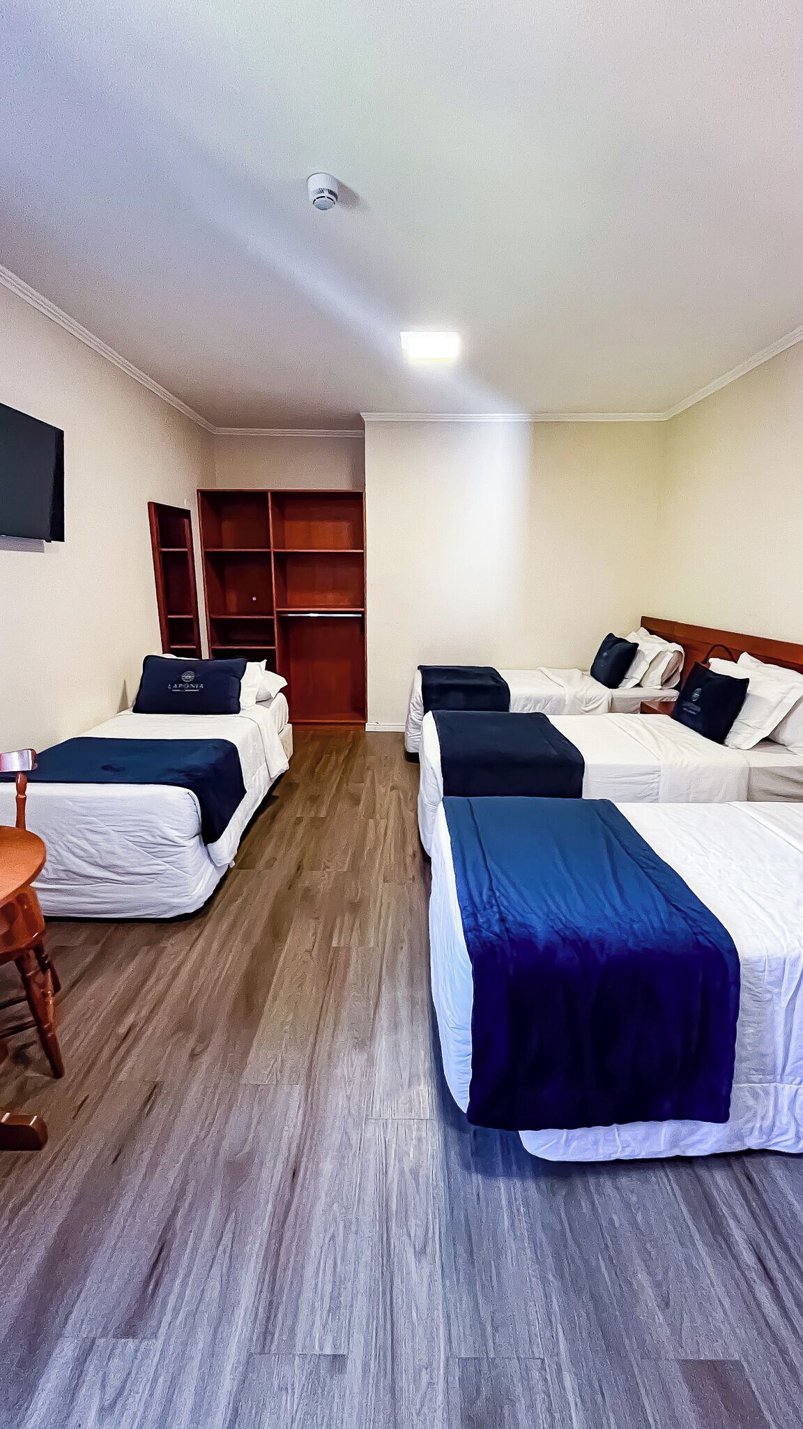 A hotel room with four beds, a wooden floor, a TV on the wall, and a wardrobe.