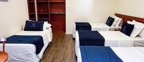 A hotel room with four beds, a wooden floor, a TV on the wall, and a wardrobe.